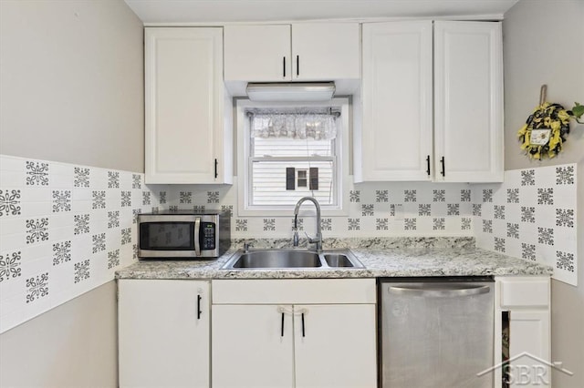 kitchen featuring a sink, light stone counters, tasteful backsplash, stainless steel appliances, and white cabinets