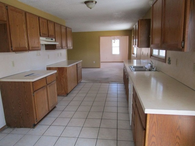 kitchen with under cabinet range hood, light countertops, brown cabinetry, and a sink