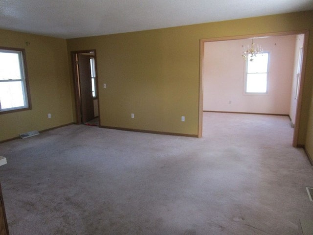 spare room featuring visible vents, light carpet, baseboards, and a chandelier