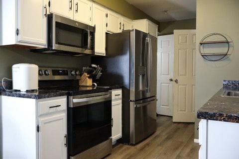 kitchen with stainless steel appliances, dark countertops, wood finished floors, and white cabinetry