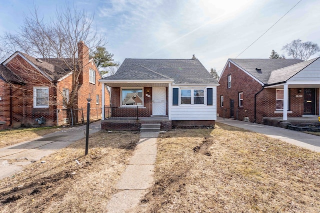 bungalow featuring covered porch, a shingled roof, and fence