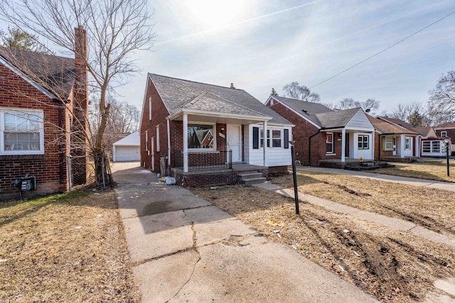 bungalow featuring a garage, brick siding, a porch, and an outdoor structure