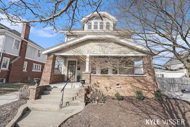 american foursquare style home featuring brick siding, a porch, and fence