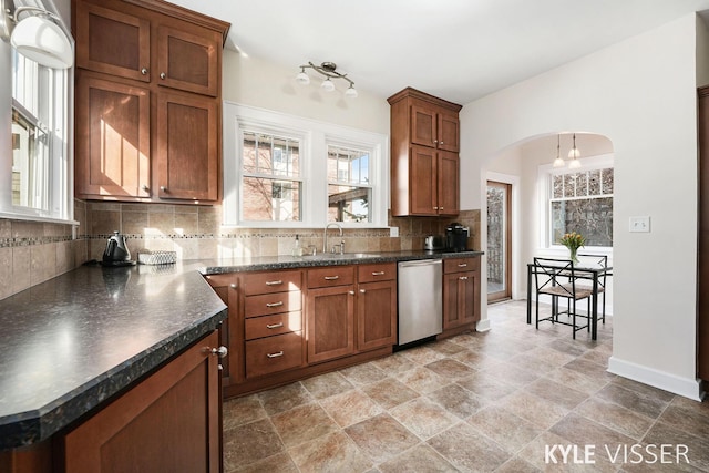 kitchen featuring a sink, backsplash, dark countertops, arched walkways, and dishwasher