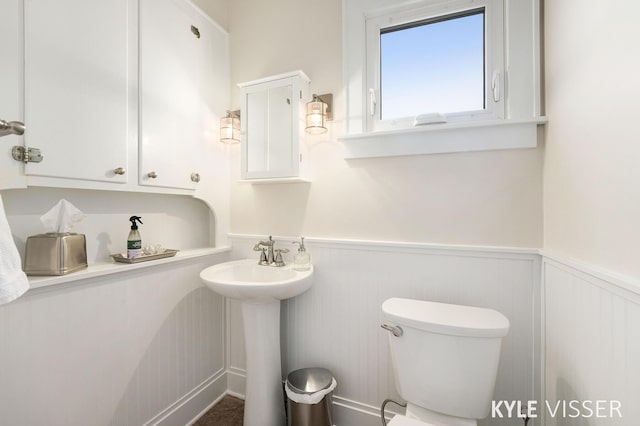 bathroom with a wainscoted wall, toilet, and a sink