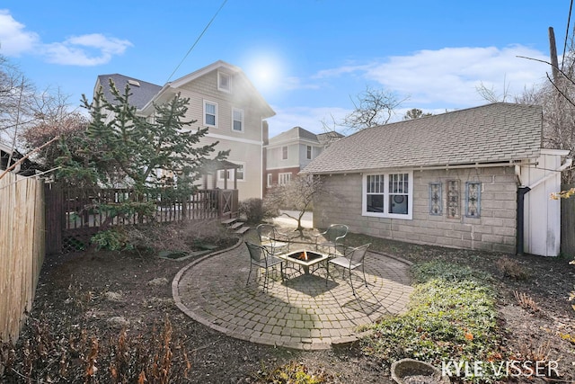 back of property featuring concrete block siding, a patio, fence, a shingled roof, and a fire pit