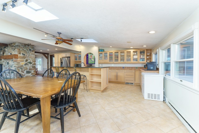 dining room featuring light tile patterned floors, baseboard heating, a skylight, and a ceiling fan