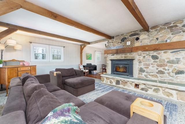 living area featuring beam ceiling, a textured ceiling, a stone fireplace, and wood finished floors