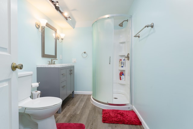 bathroom featuring vanity, wood finished floors, baseboards, a shower stall, and toilet