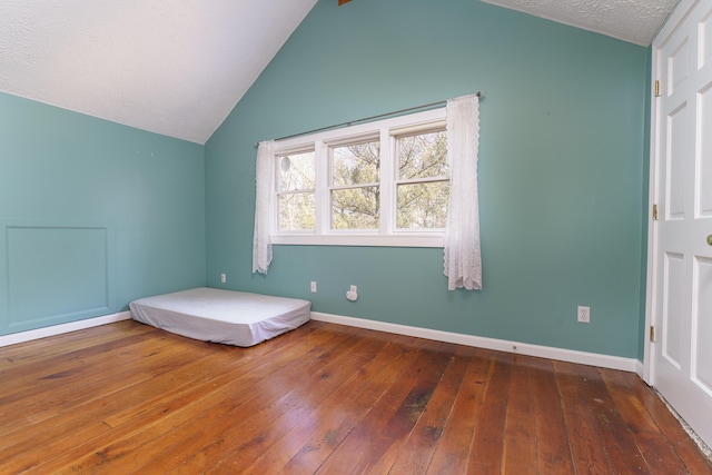 unfurnished bedroom with baseboards, wood-type flooring, a textured ceiling, and lofted ceiling