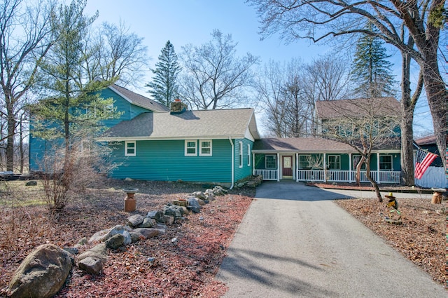 view of front facade with aphalt driveway, covered porch, roof with shingles, and a chimney