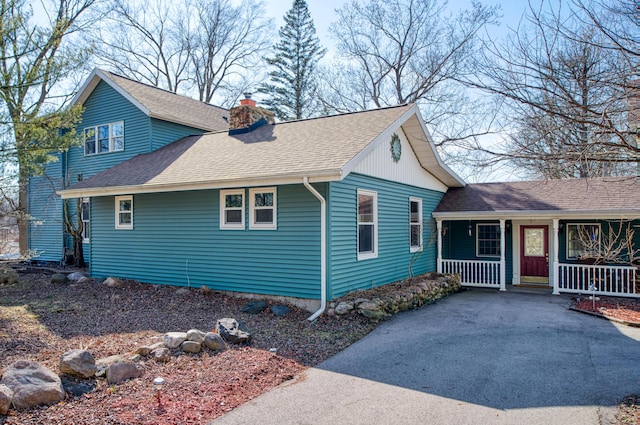 view of front of property featuring a porch, roof with shingles, driveway, and a chimney