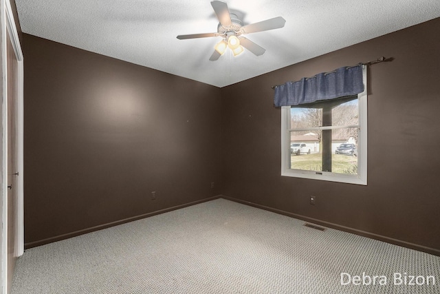 empty room with visible vents, baseboards, carpet, a textured ceiling, and a ceiling fan