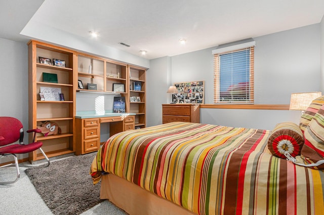 carpeted bedroom with visible vents and built in desk