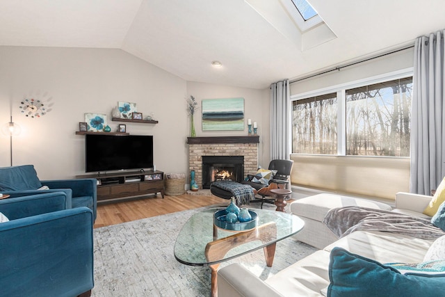 living room featuring a brick fireplace, vaulted ceiling with skylight, and wood finished floors