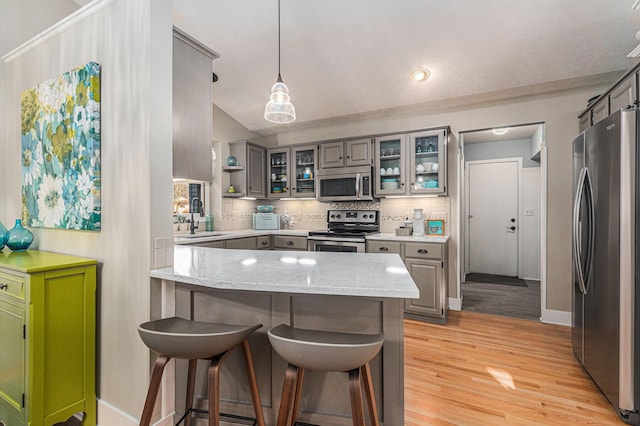 kitchen with a kitchen breakfast bar, tasteful backsplash, appliances with stainless steel finishes, a peninsula, and light wood finished floors