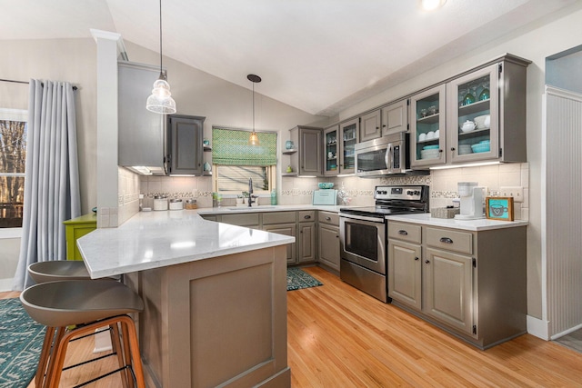 kitchen with lofted ceiling, a peninsula, light wood-style flooring, gray cabinetry, and appliances with stainless steel finishes