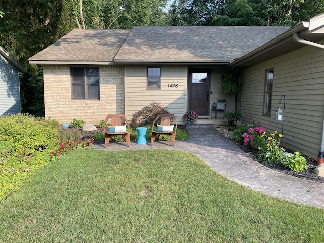 back of house with a yard, brick siding, and a shingled roof