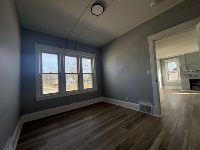 empty room with visible vents, a brick fireplace, baseboards, and wood finished floors