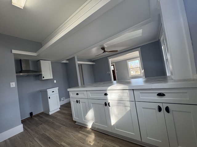 kitchen with baseboards, white cabinets, wall chimney exhaust hood, a ceiling fan, and dark wood-style flooring