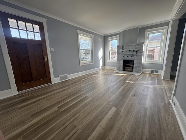 unfurnished living room with visible vents, a brick fireplace, crown molding, baseboards, and dark wood finished floors