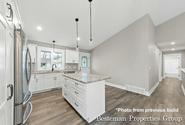 kitchen with visible vents, lofted ceiling, freestanding refrigerator, wood finished floors, and a sink