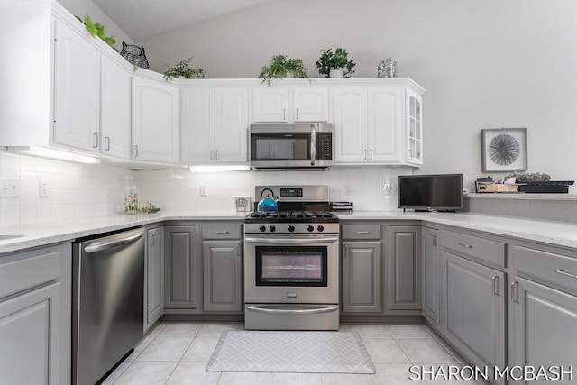 kitchen featuring stainless steel appliances, gray cabinetry, light tile patterned flooring, and vaulted ceiling