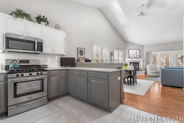 kitchen featuring gray cabinetry, white cabinetry, stainless steel appliances, a peninsula, and a fireplace