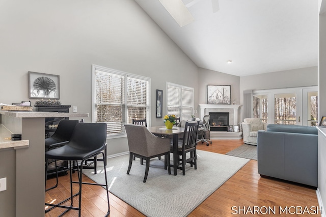 dining space with baseboards, light wood-style floors, a glass covered fireplace, and high vaulted ceiling