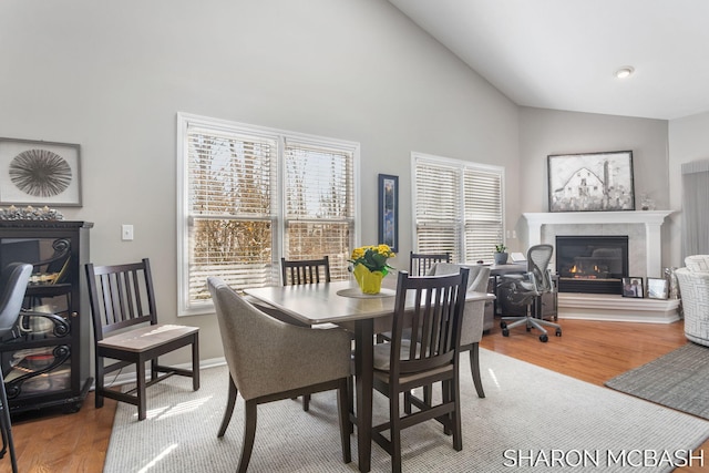 dining room with baseboards, wood finished floors, high vaulted ceiling, and a glass covered fireplace