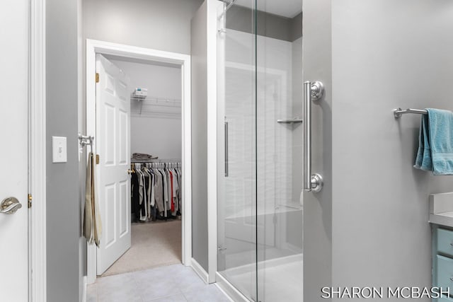 full bath with tile patterned floors, a walk in closet, a stall shower, and vanity