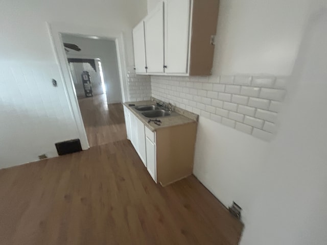 kitchen with light countertops, decorative backsplash, wood finished floors, white cabinetry, and a sink