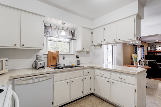 kitchen with a sink, white appliances, a peninsula, white cabinets, and light countertops