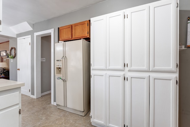 kitchen featuring white cabinets, white refrigerator with ice dispenser, and light countertops