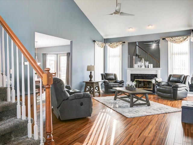 living area with wood finished floors, a premium fireplace, high vaulted ceiling, ceiling fan, and stairs