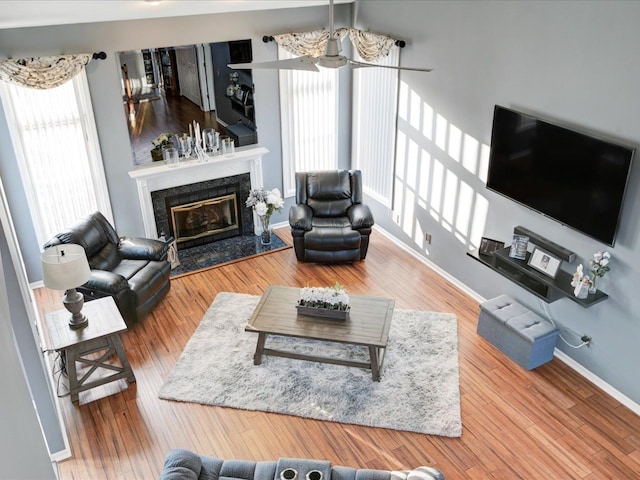 living area featuring a ceiling fan, wood finished floors, baseboards, and a premium fireplace