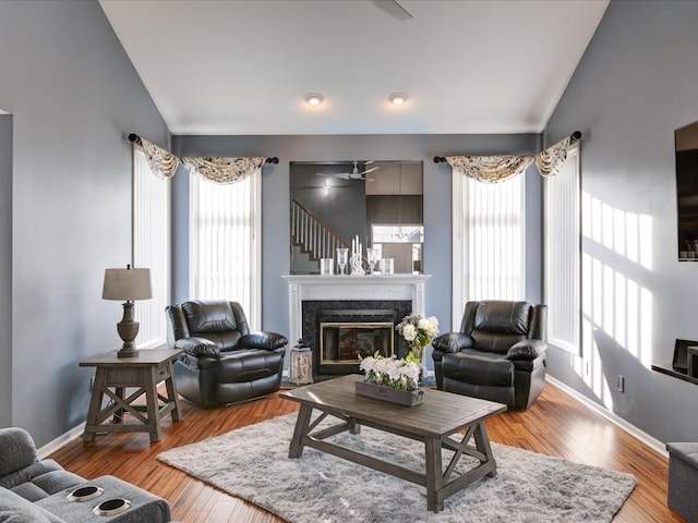 living area with a fireplace, wood-type flooring, baseboards, and vaulted ceiling