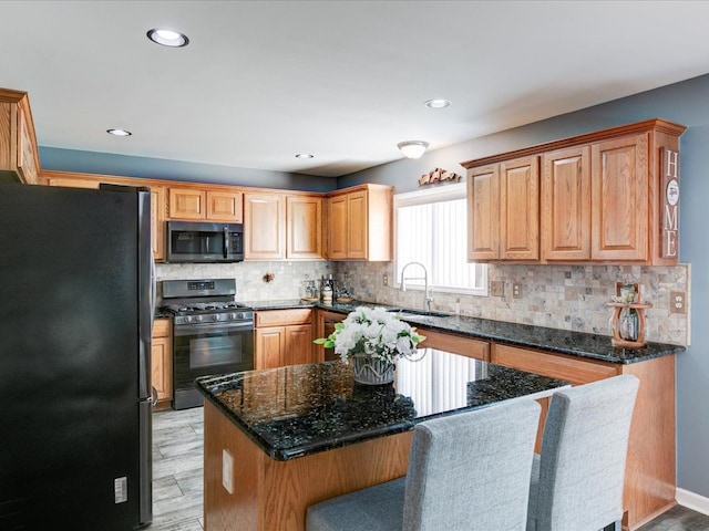 kitchen featuring backsplash, black range with gas cooktop, freestanding refrigerator, and a sink