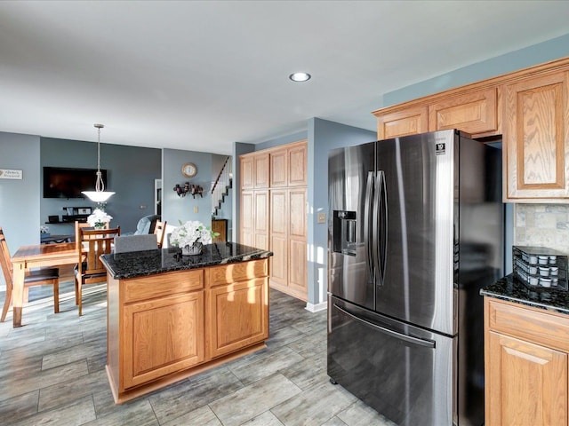 kitchen with dark stone countertops, decorative backsplash, a kitchen island, and stainless steel fridge with ice dispenser