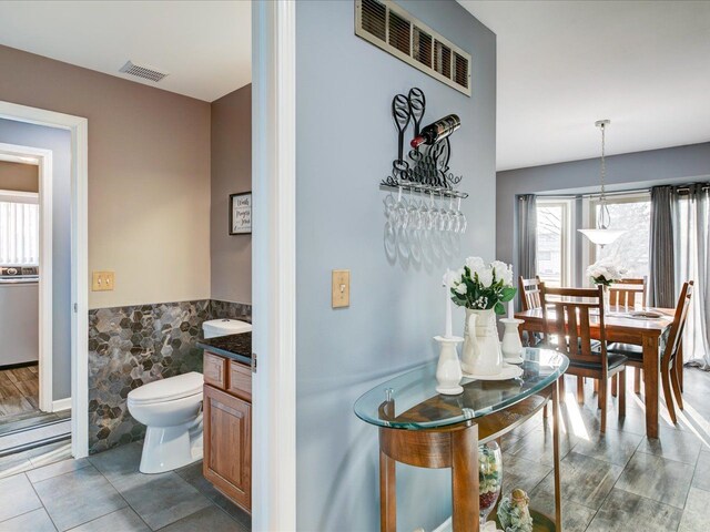 interior space featuring visible vents, toilet, tile walls, and a wainscoted wall