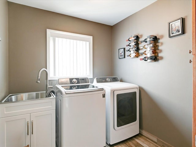 laundry area featuring light wood-style flooring, cabinet space, independent washer and dryer, and a sink