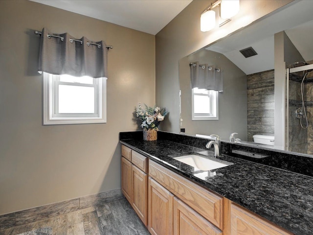 bathroom featuring baseboards, toilet, a tile shower, wood finished floors, and vanity