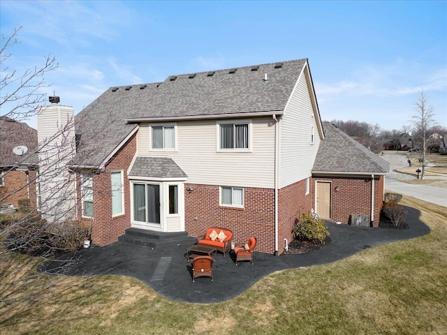 back of property with brick siding, a shingled roof, entry steps, a lawn, and a chimney