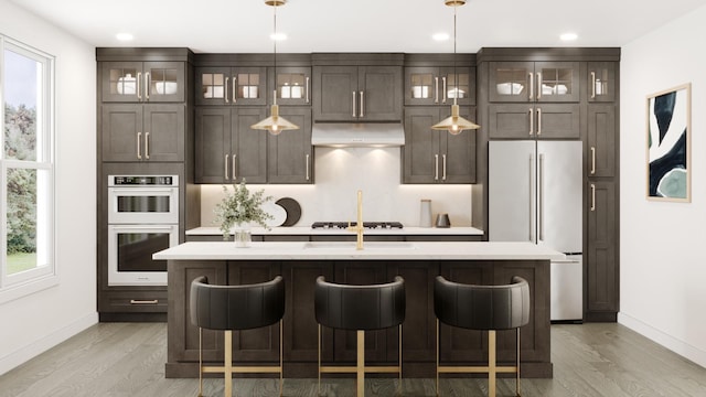 kitchen with a center island with sink, stovetop, high end fridge, under cabinet range hood, and double oven