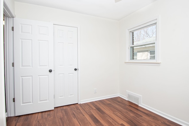 unfurnished bedroom with a closet, baseboards, visible vents, and dark wood-style flooring