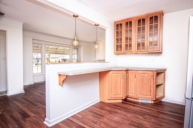 kitchen with glass insert cabinets, a peninsula, light countertops, and dark wood-type flooring