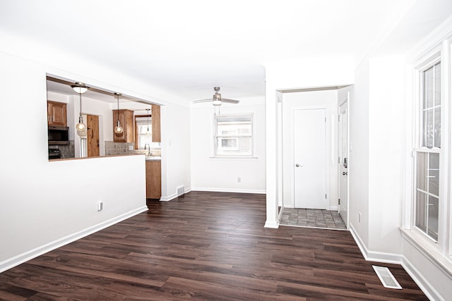 unfurnished living room featuring baseboards, visible vents, dark wood-style flooring, a sink, and ceiling fan