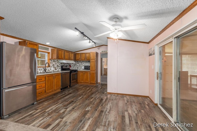 kitchen featuring dark wood-type flooring, a sink, appliances with stainless steel finishes, brown cabinetry, and lofted ceiling