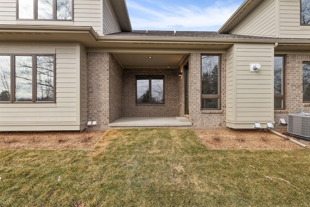 property entrance featuring brick siding, central air condition unit, and a lawn