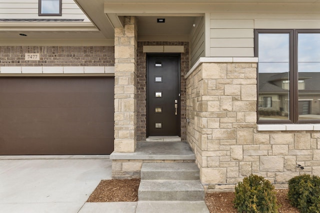 doorway to property featuring stone siding, elevator, concrete driveway, a garage, and brick siding